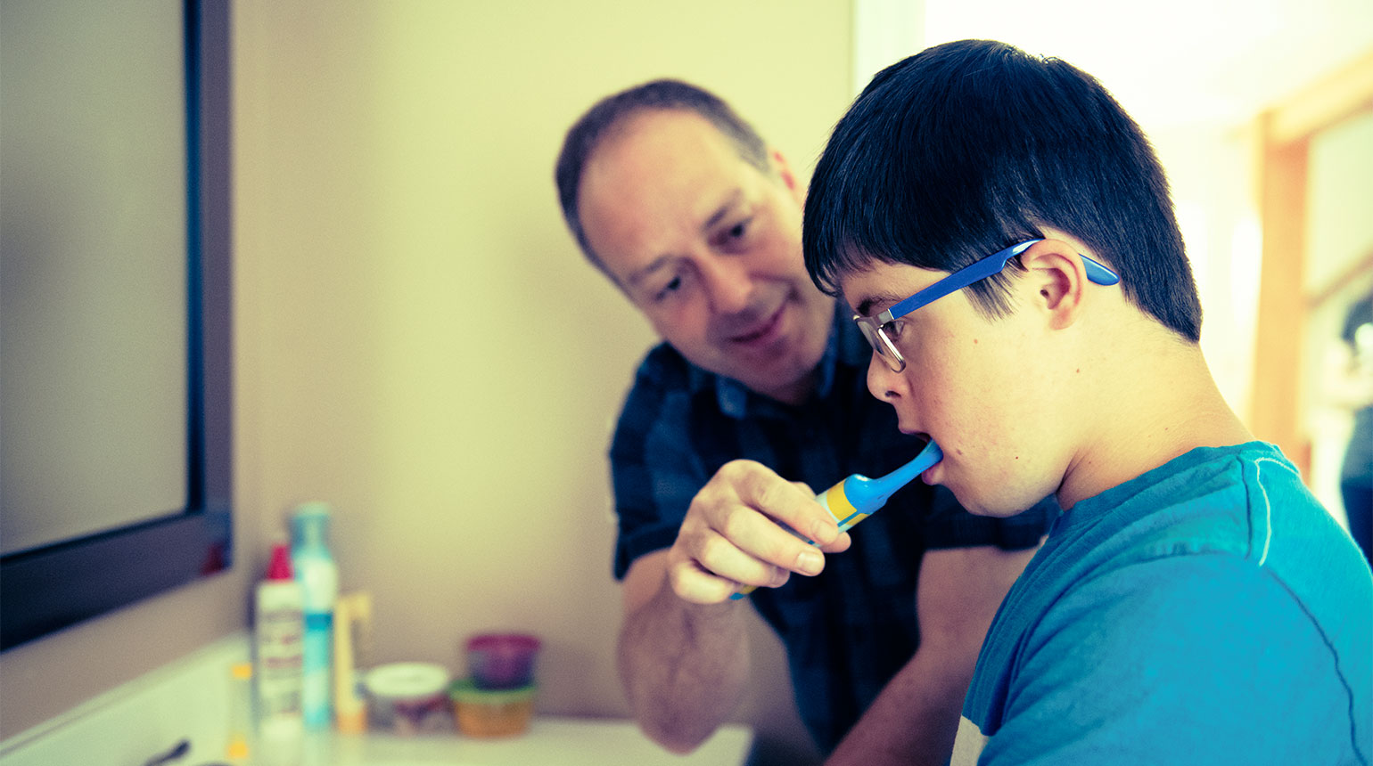 Ein Mann putzt einem Jungen mit geistiger Behinderung die Zähne.